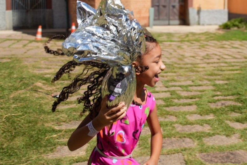 Criança celebra vitória com ovo de Páscoa gigante na "Caça aos Ovos" na Brasital. Alegria e surpresa marcam evento.