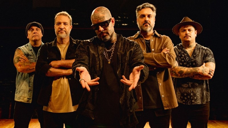 Banda posa para foto promocional do São Rock Music Fest 2026. Integrantes aparecem com roupas casuais, alguns com tatuagens e acessórios. Fundo escuro.