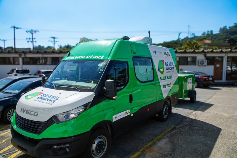 Unidade odontológica móvel do programa "Brasil Sorridente" estacionada. Veículo verde e branco oferece serviços de saúde bucal à população.