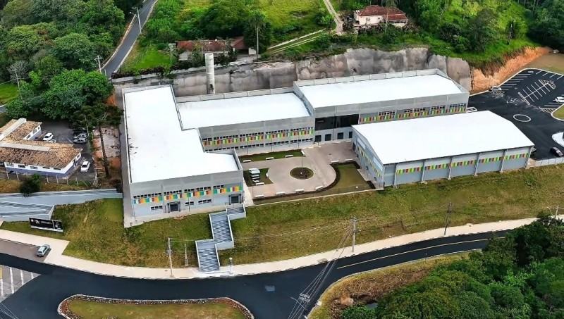 Vista aérea da Escola do Futuro em São Roque, com arquitetura moderna e estacionamento. A escola se destaca em meio à área verde.