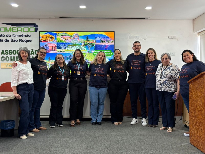 Equipe posa para foto após a conclusão do Diagnóstico Socioterritorial de São Roque. Ao fundo, tela com informações e logo da cidade.
