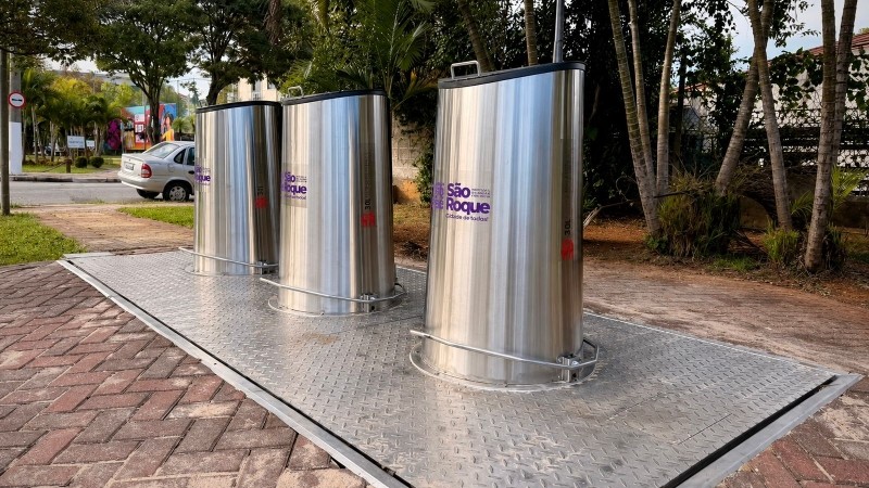 Lixeiras subterrâneas instaladas em São Roque. Na imagem, três coletores de lixo em aço inoxidável sobre plataforma metálica, com identificação da prefeitura.